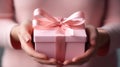 Close-up of delicate hands presenting a pink gift box with a satin ribbon, symbolizing care and generosity for a special occasion