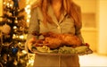 Close-up of delicious baked Christmas duck with apples and herbs. Girl in pajamas holds festive dish against background of