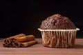Close up of a delicious chocolate muffin with cinnamon sticks on a wooden table against black background. Space for text