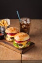 Close-up of delicious fresh home made burger with lettuce, cheese, onion and tomato on a rustic wooden board. Also fries and Cola Royalty Free Stock Photo