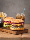 Close-up of delicious fresh home made burger with lettuce, cheese, onion and tomato on a rustic wooden board. Also fries and Cola Royalty Free Stock Photo