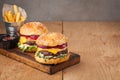 Close-up of delicious fresh home made burger with lettuce, cheese, onion and tomato on a rustic wooden board. Also fries and Cola Royalty Free Stock Photo