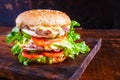 Close-up of delicious fresh home made burger with lettuce, cheese, onion and tomato on a rustic wooden plank on wooden table Royalty Free Stock Photo