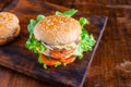 Close-up of delicious fresh home made burger with lettuce, cheese, onion and tomato on a rustic wooden plank on wooden table Royalty Free Stock Photo