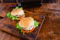 Close-up of delicious fresh home made burger with lettuce, cheese, onion and tomato on a rustic wooden plank on wooden table Royalty Free Stock Photo