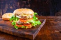 Close-up of delicious fresh home made burger with lettuce, cheese, onion and tomato on a rustic wooden plank on wooden table Royalty Free Stock Photo