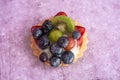 Close up of a delicious fruit tart with blueberries kiwi strawberries grapes and raspberries on a light purple background Royalty Free Stock Photo