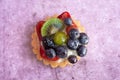 Close up of a delicious fruit tart with blueberries kiwi strawberries grapes and raspberries on a light purple background Royalty Free Stock Photo