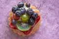 Close up of a delicious fruit tart with blueberries kiwi strawberries grapes and raspberries on a light purple background Royalty Free Stock Photo