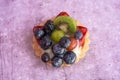 Close up of a delicious fruit tart with blueberries kiwi strawberries grapes and raspberries on a light purple background Royalty Free Stock Photo