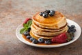 Close-up delicious pancakes, with fresh blueberries, strawberries and maple syrup on a rusty background. With copy space Royalty Free Stock Photo