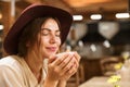 Close up of a delighted girl in hat sitting at the cafe table indoor