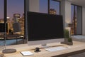 Close up of designer office desktop with empty black computer monitor, window with night city view, decorative items and supplies Royalty Free Stock Photo