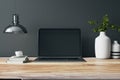 Close up of designer office interior with various objects, coffee cup and empty mock up place on laptop computer monitor. Wooden