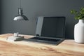 Close up of designer office interior with various objects, coffee cup and empty mock up place on laptop computer screen. Wooden