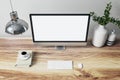 Close up of designer office interior with various objects, coffee cup and empty mock up place on white computer monitor. Wooden