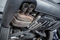 Close-up detail bottom view of car part metal exhaust muffler pipe with rusty stains. Lifted vehicle check-up maintenace