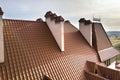 Close-up detail of building steep shingle roof and brick plastered chimneys on house top with metal tile roof. Roofing, repair and Royalty Free Stock Photo