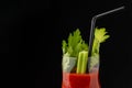 Close-up detail of crystal glass with bloody mary cocktail, celery and black straw, on black background, horizontal,