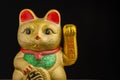 Close-up detail of golden maneki neko with green and red tones, black background, horizontal,