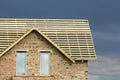 Close-up detail of new brick house top with two narrow plastic attic windows and wooden roof frame under construction on dark blue Royalty Free Stock Photo