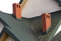 Close-up detail of new modern house top with shingled green roof, high brick-red chimneys and stucco walls. Professionally done bu