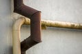 Close-up detail of old dirty painted yellow natural gas and brown gutter rain water pipes fastened to white house wall. Safety, da