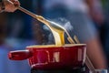 Close up detail shot of person's arm stirring a traditional tasty delicious pot of hot melted liquid swiss cheese fondue