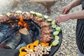 Close-up detail view of chef flipping by tongs tasty crispy marinated quails and vegetables grilled at round steel iron