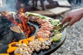 Close-up detail view of chef flipping by tongs tasty crispy marinated quails and vegetables grilled at round steel iron