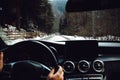 Close up details of driver driving a modern car. Inside of car details, drivers view through windshield. Winter mountain landscape