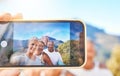 Close up of device screen while active senior people pose together for a selfie outdoors. Group of mature people