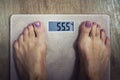 Close up of digital bathroom scale with female bare feet on it showing 55,5 kilogram on display. Woman standing on