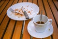 Close up dirty coffee cup and spoon setting on white saucer, knife and fork on white dirty dish. They are on wooden table. Royalty Free Stock Photo