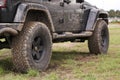 Close up of dirty Jeep Wrangler after driving heavy off-road in wet terrain. Wheels soiled in mud and dirt. Standing on green gras