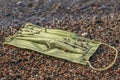 Close-up of a discarded used face mask lies in the surf zone on a sandy pebble beach. Budva, Montenegro Royalty Free Stock Photo