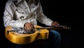 Close-up of a Dobro guitar resting on the lap of a musician dressed in cowboy attire on dark backdrop