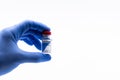 Close-up of a doctor`s hand with blue glove holding a vial of COVID-19 vaccine on white background