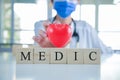 Close-up doctor in uniform wearing a face mask with a stethoscope and hold red heart with wood cubes word MEDIC Royalty Free Stock Photo