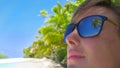 CLOSE UP: Detailed shot of reflection of a palm tree in girl's dark sunglasses.