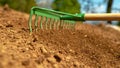 CLOSE UP: Green metal rake is being pulled through dry soil ready for planting.