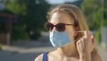 CLOSE UP: Young Caucasian woman wearing sunglasses takes off her facemask. Royalty Free Stock Photo