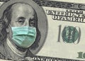 A close up of a 100 dollar bill shows Benjamin Franklin wearing a surgical mask