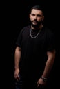 Close-up of a dramatic portrait of a young serious guy, musician, singer, rapper with a beard in black clothes on a black isolated