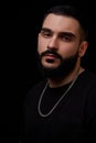 Close-up of a dramatic portrait of a young serious guy, musician, singer, rapper with a beard in black clothes on a black isolated