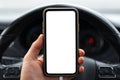 Close-up of driver man hand holding modern smartphone with white mockup on screen, background of car steering wheel. Royalty Free Stock Photo