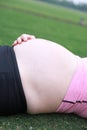 Close-up of Eastern Asian Chiense pregnant woman`s belly, lying on grass meadow field enjoy free casual time in nature outdoor Royalty Free Stock Photo