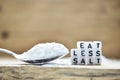 Close-up of Eat less salt text written with plastic letters near a salt spoon