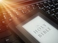 Close up of ebook reader with The Holy Bible on a laptop keyboard, with sun rays light concept Royalty Free Stock Photo