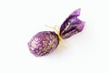 Close-up egg or ellipse shaped candy wrapped in puprle and golden paper with bow. Gift, souvenir, some sweets or traditional treat